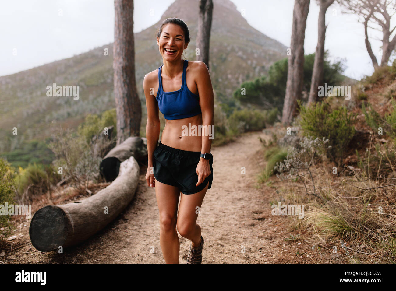 Shot de beautiful young asian woman standing on mountain trail et rire. Coureuse en bonne santé dans les vêtements de sport sur chemin. Banque D'Images
