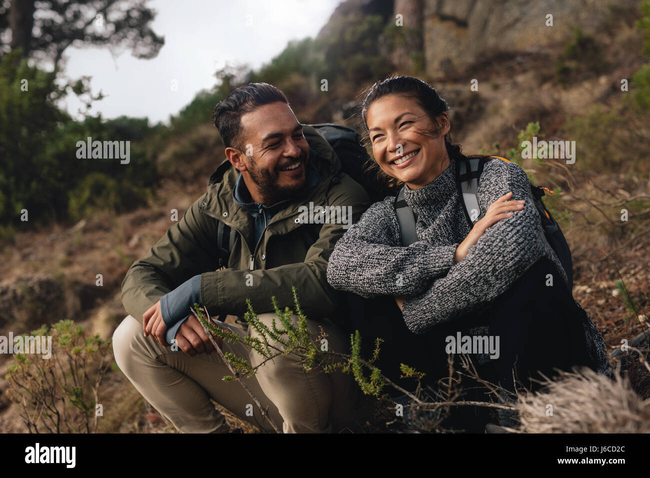 Jeune couple en faisant une pause sur une randonnée. Heureux jeune homme et femme assis sur sentier de montagne. Banque D'Images