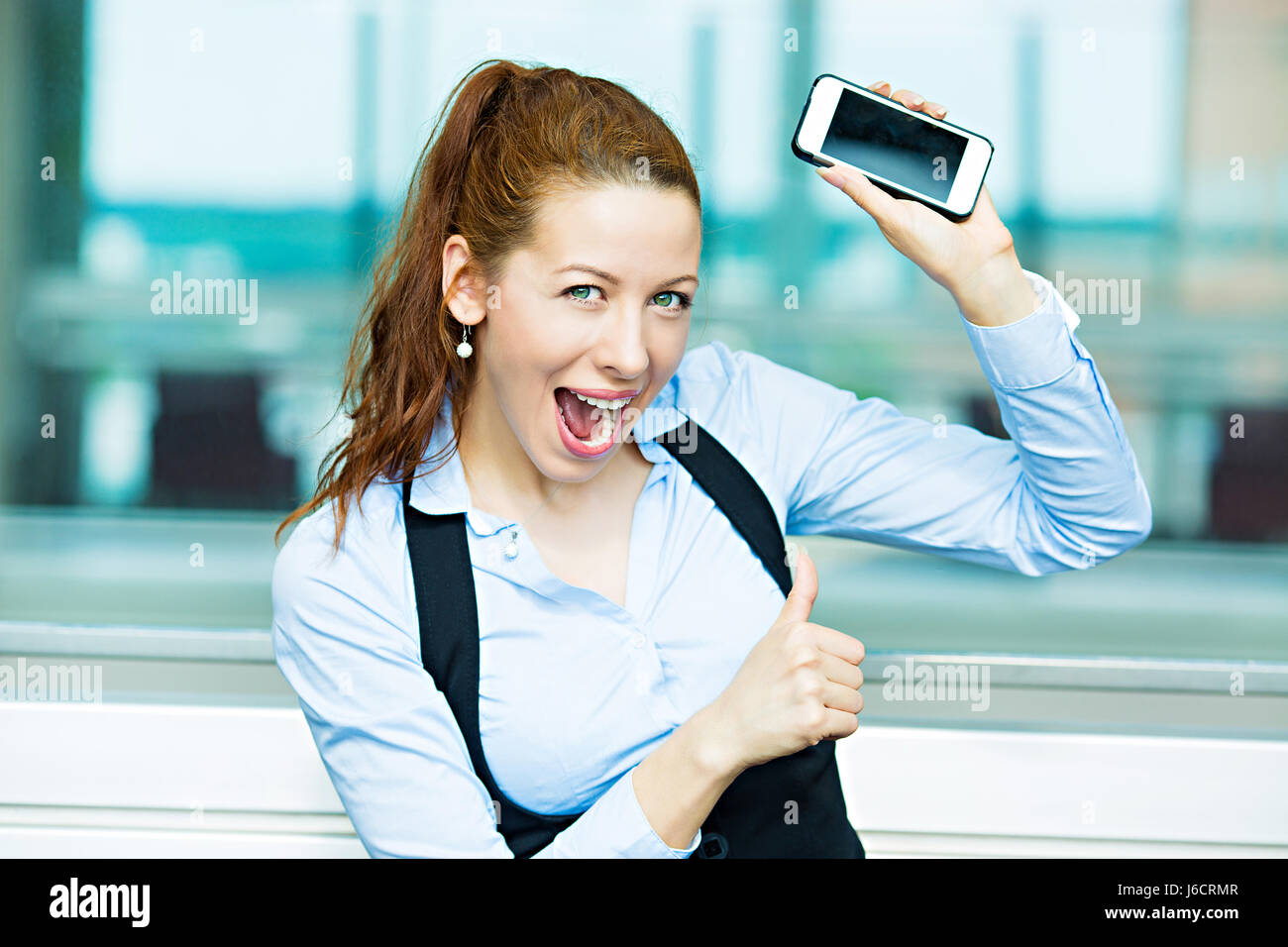 Closeup portrait heureux, heureux, jeune, jolie femme d'affaires, employé de l'entreprise montrant, tenant son téléphone intelligent, giving Thumbs up, isolé backg Banque D'Images