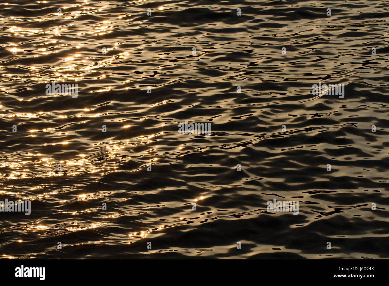 Image complète de la surface d'un océan calme la nuit avec lumière du soleil orange clignotantes sur la surface miroitante de la nature dans une image d'arrière-plan. Banque D'Images