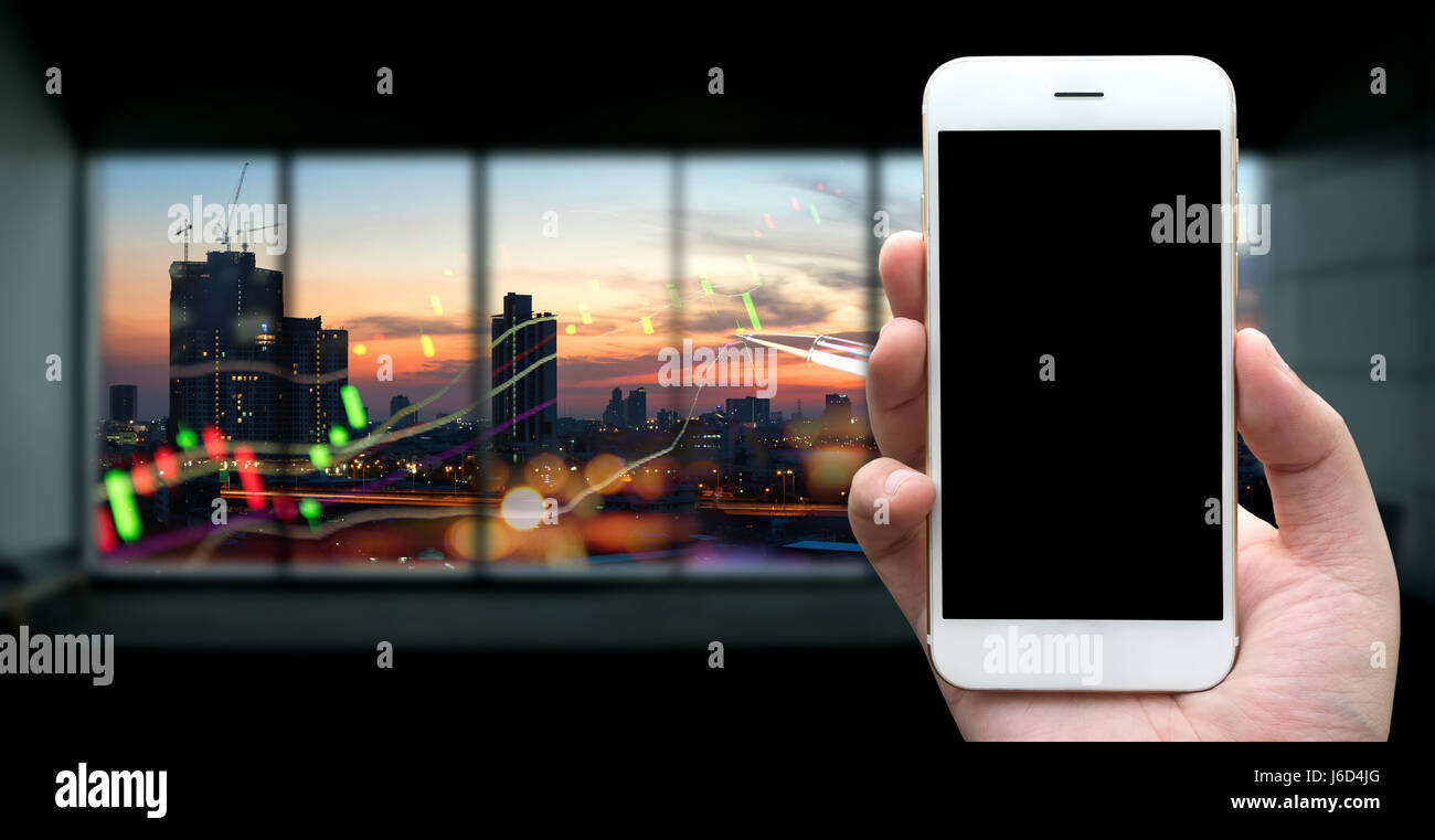 Fintech ,et Forex bourse concept. Human hand holding blanc téléphone sur un écran noir avec le coucher du soleil et la ville en arrière-plan graphique stock technique Banque D'Images