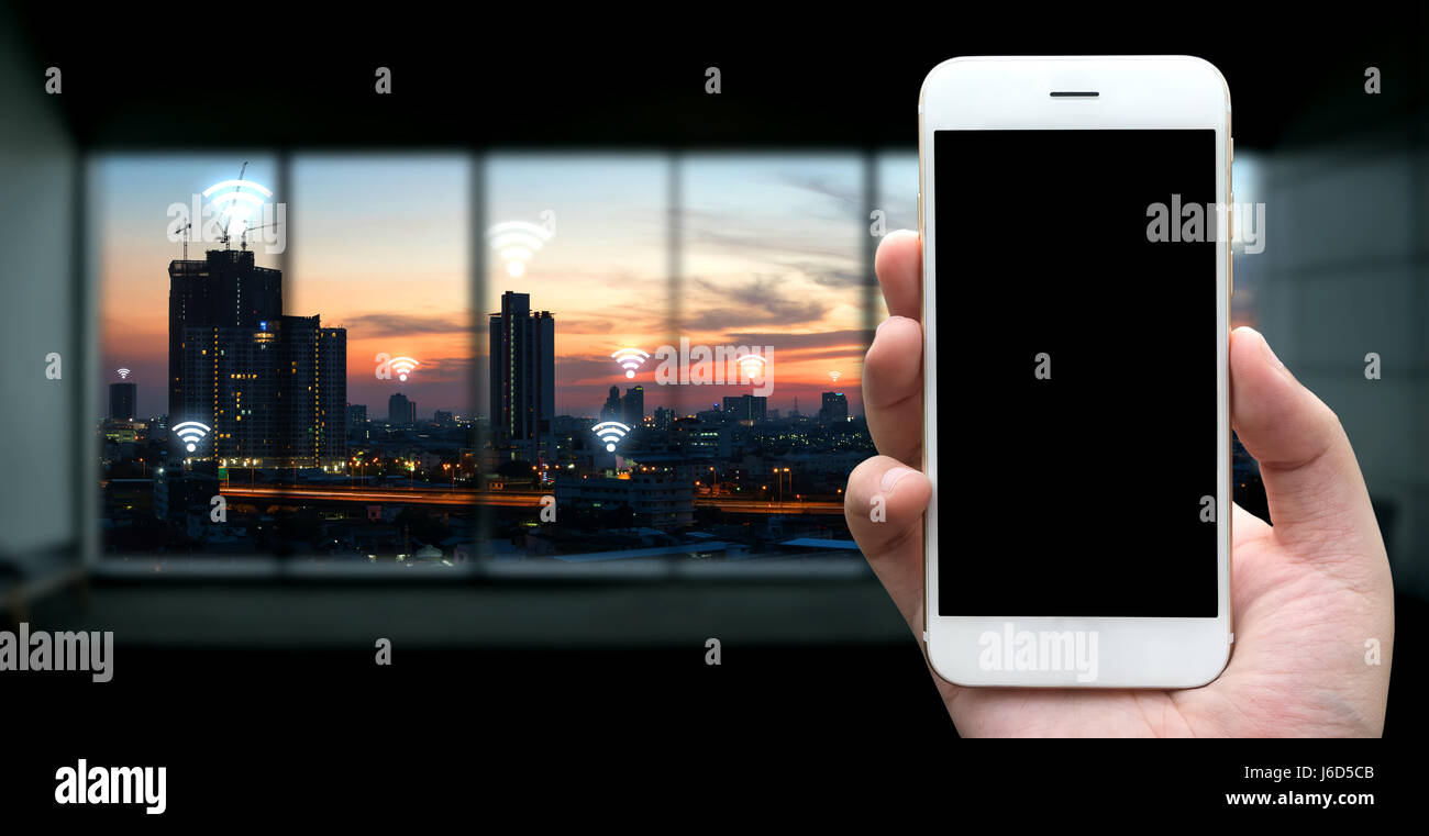 Internet des objets , l'Ito et réseau connexion concept. Businessman hand holding blanc téléphone et écran noir avec fond coucher de ville et icônes wifi Banque D'Images