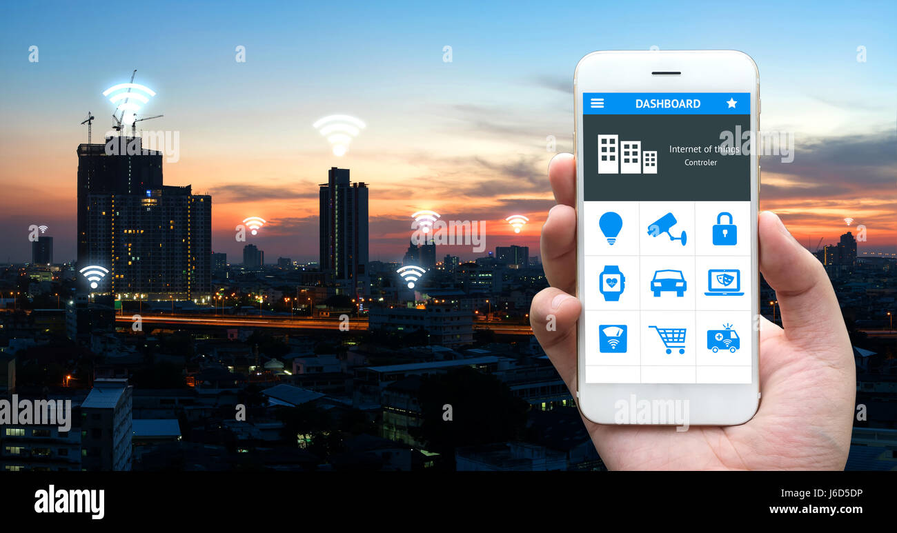 Internet des objets , iot , smart home , des ville et réseau connexion concept. Human hand holding blanc téléphone et l'application avec city sunset view b Banque D'Images