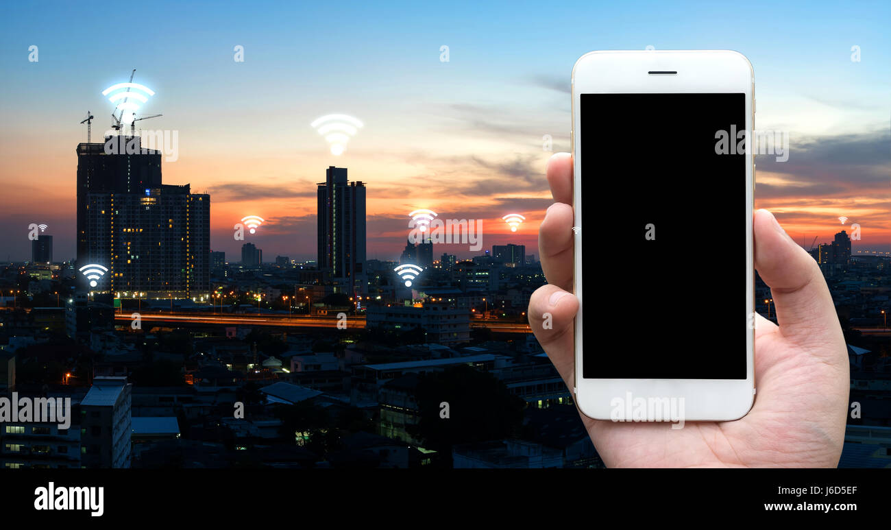 Internet des objets , l'Ito et réseau connexion concept. Businessman hand holding tablet noir fond coucher de soleil sur la ville et connexion Wi-Fi gratuite icônes Banque D'Images