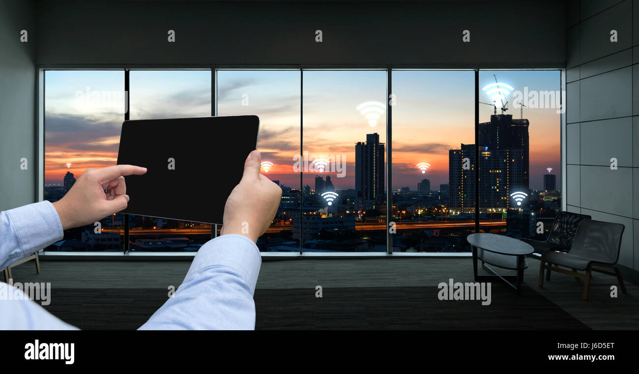 Internet des objets , l'Ito et réseau connexion concept. Businessman hand holding tablet noir fond coucher de soleil sur la ville et connexion Wi-Fi gratuite icônes Banque D'Images