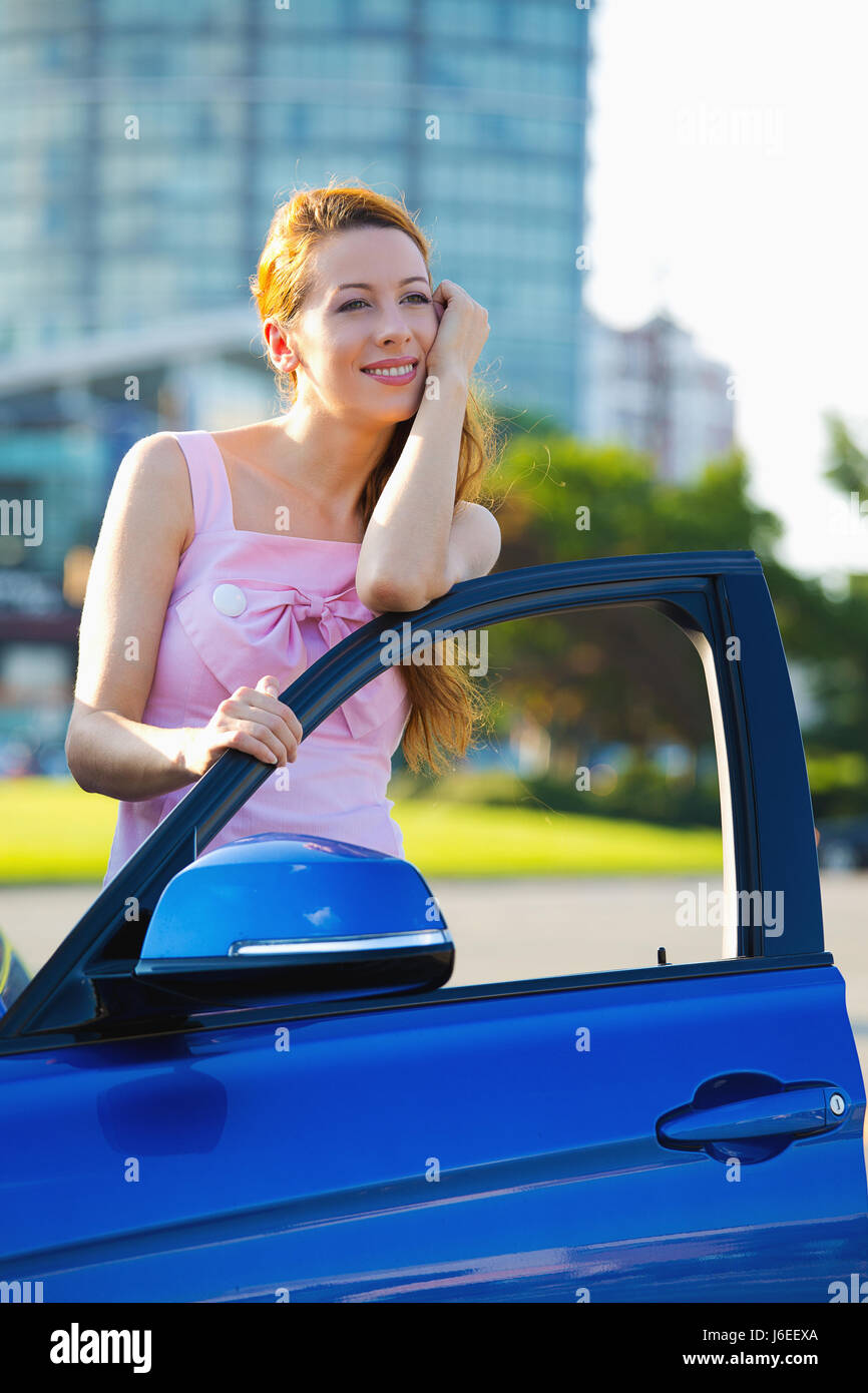 Portrait of happy smiling young attractive woman acheteur debout à côté de sa nouvelle voiture bleue à l'extérieur isolé concessionnaire revendeur lot corporate office background Banque D'Images