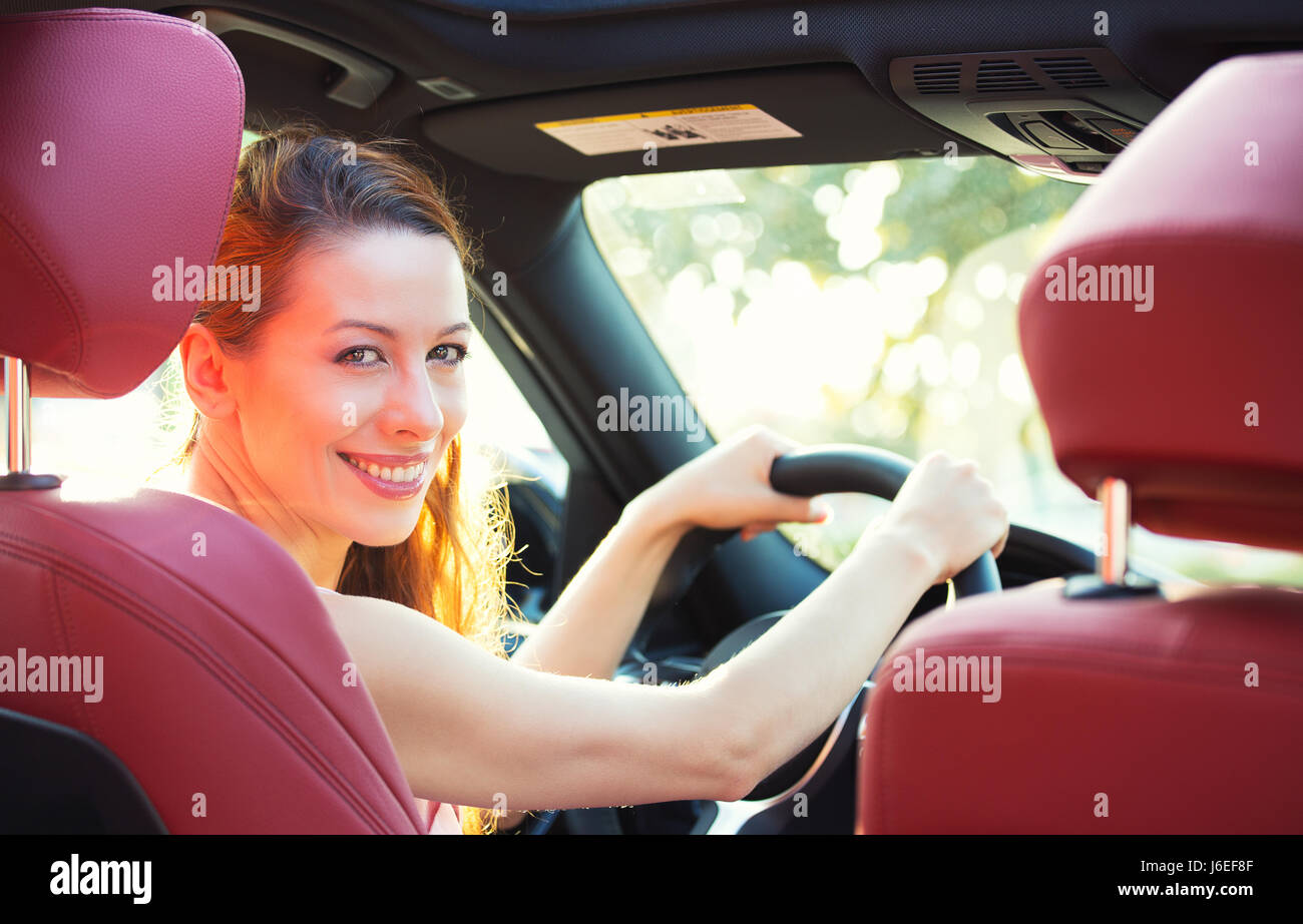 Portrait femme heureuse dans la nouvelle voiture, une roue permet, en tournant autour, souriant à la recherche, à parler aux passagers assis dans le siège arrière droit demande directi Banque D'Images