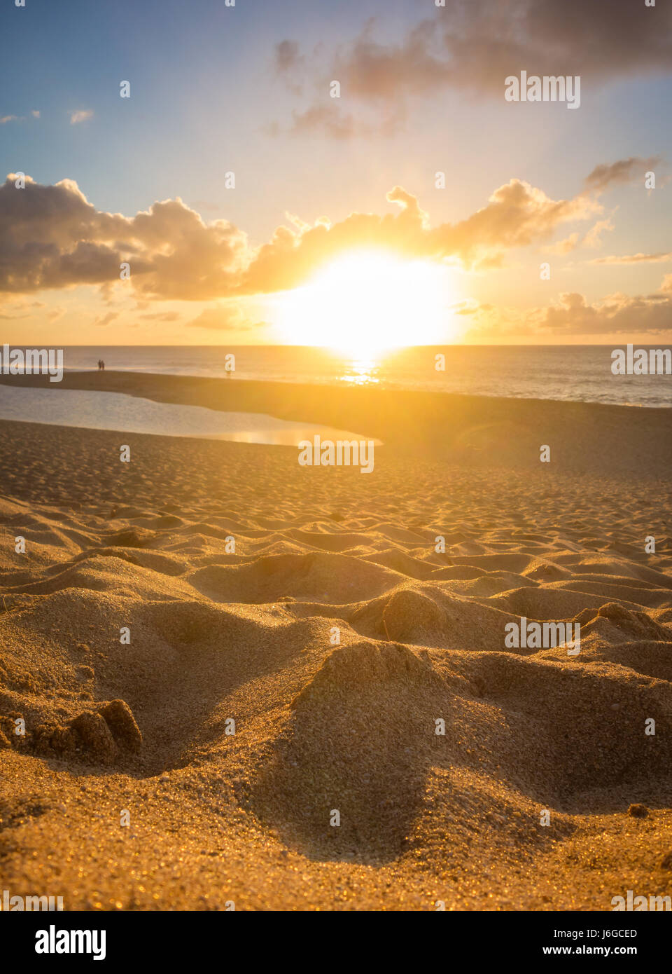 De petites dunes de sable doré brillant au soleil comme les gens dans la distance regarder le coucher de soleil sur l'océan. Banque D'Images