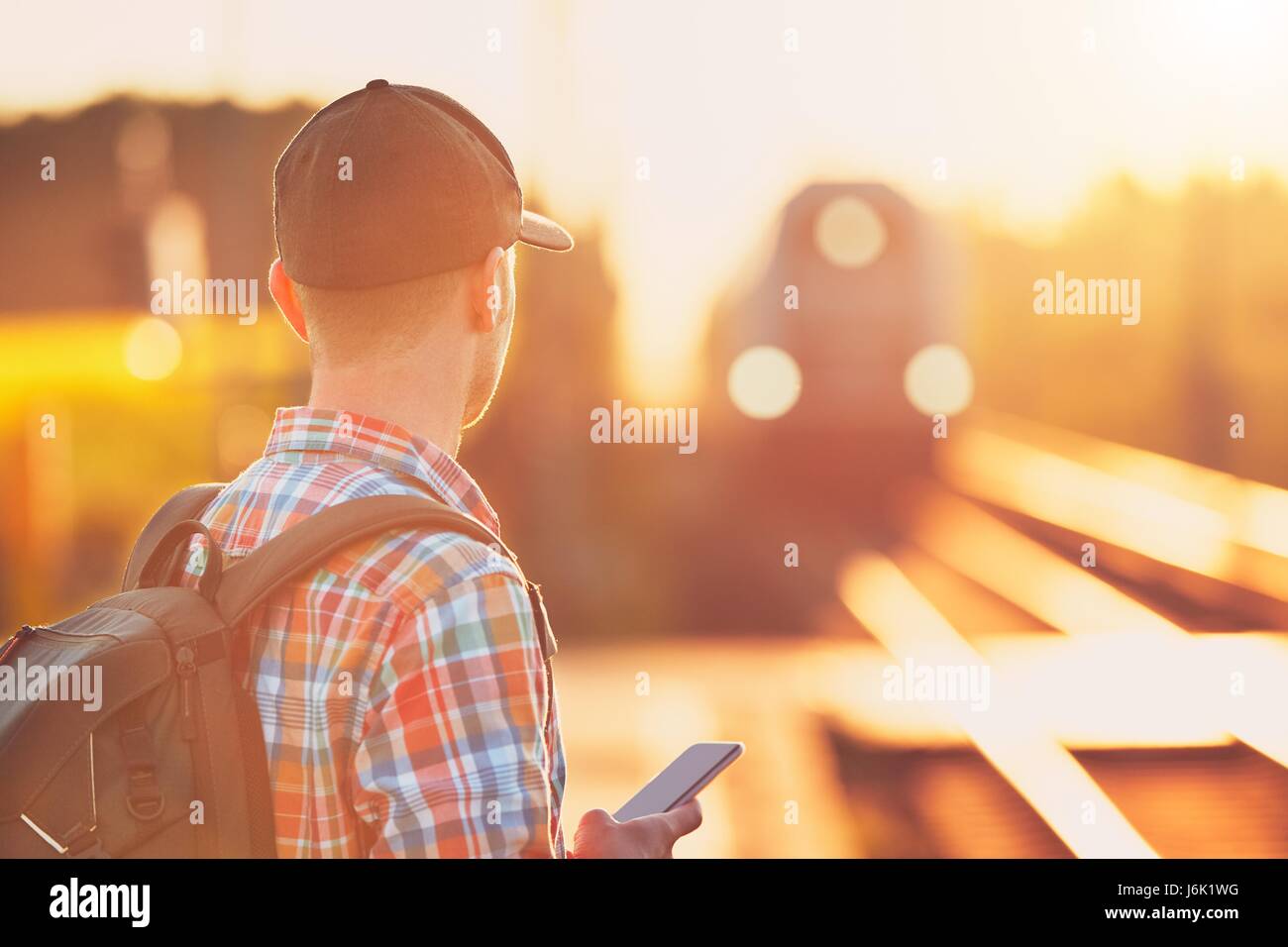 Jeune homme voyageant avec un billet électronique par train. Gare à coucher du soleil doré. Banque D'Images