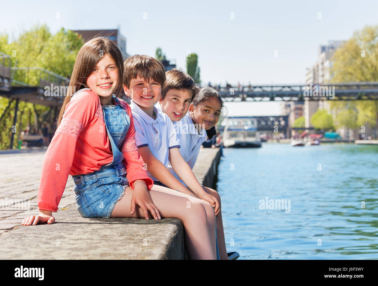 Portrait de quatre enfants multiethniques, de 10 à 12 ans garçons et filles, assis dans une ligne sur le quai en été Banque D'Images