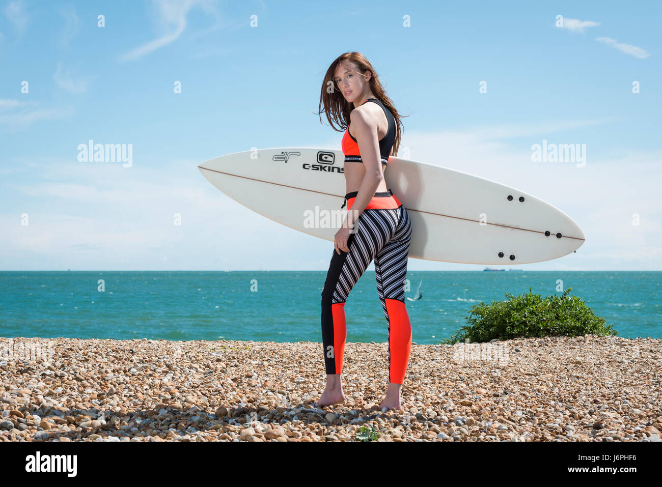 Surfer Girl portant une combinaison en néoprène transportant un surf,marche vers le haut de la plage. Banque D'Images
