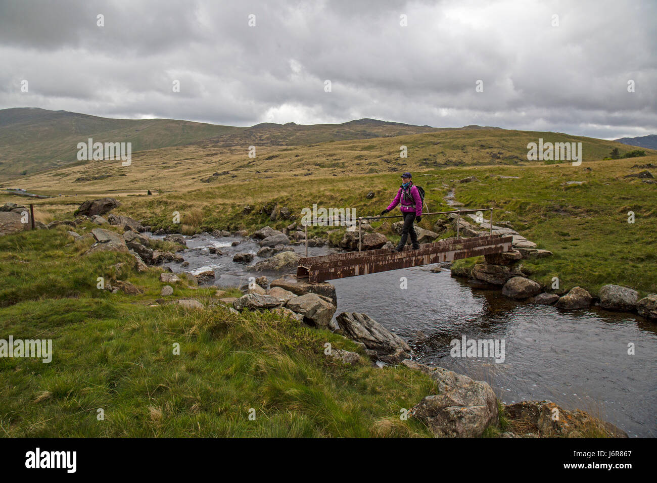 Seule femme walker pour traverser un petit pont sur un chemin vers le bas des pentes sud du planeur Fach dans le Parc National de Snowdonia, le Nord du Pays de Galles. Banque D'Images
