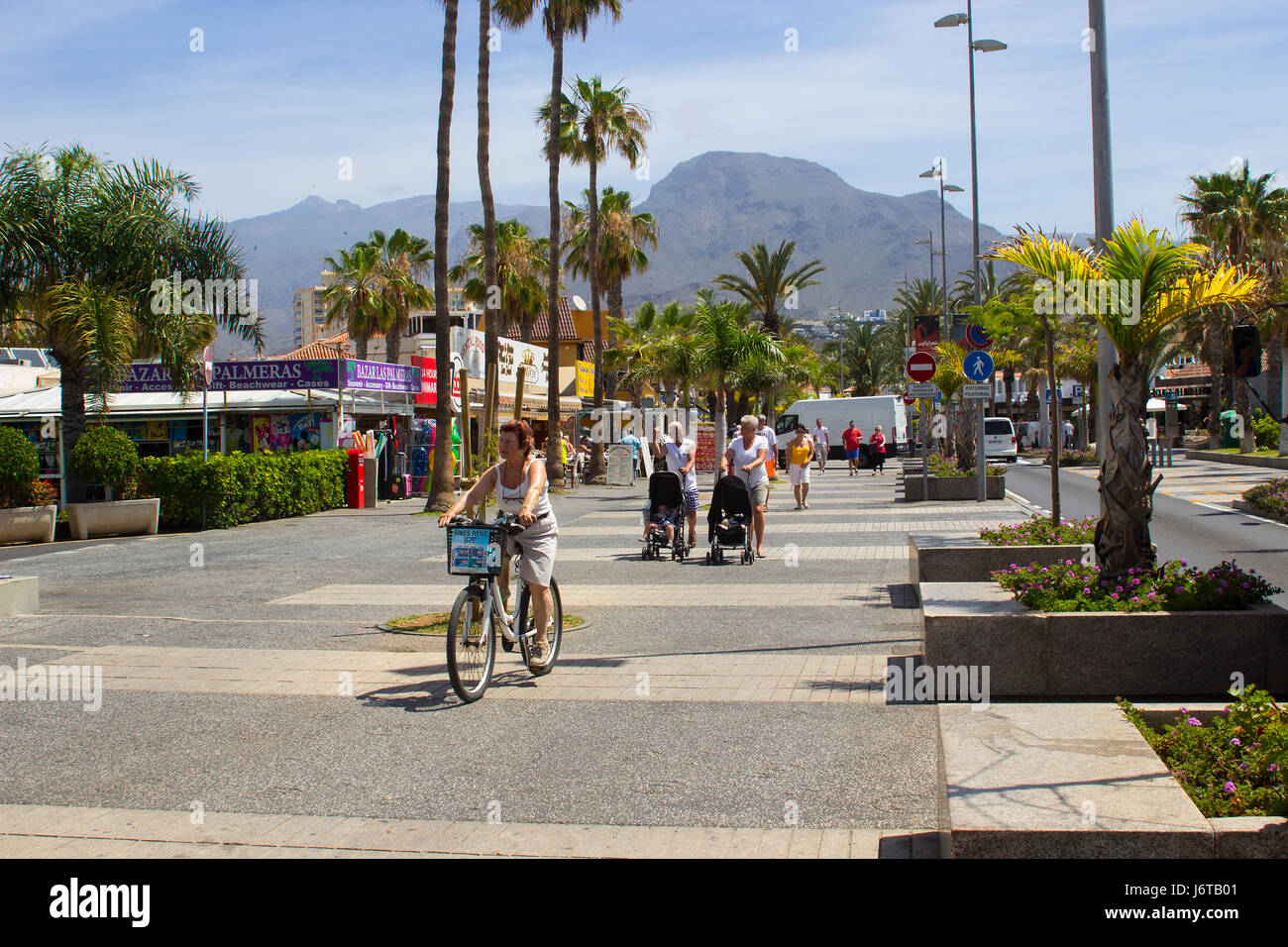 Les touristes à pied et à vélo sur une avenue bordée d'arbres avec des boutiques et des cafés à Playa de Las Americas, sur l'île de Ténériffe Banque D'Images