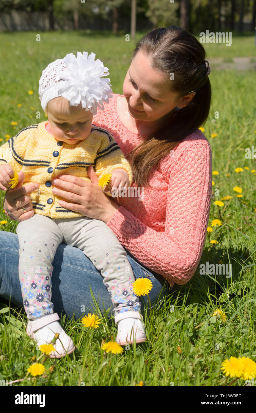 Maman et sa fille assis sur l'herbe verte avec des fleurs jaunes. Banque D'Images