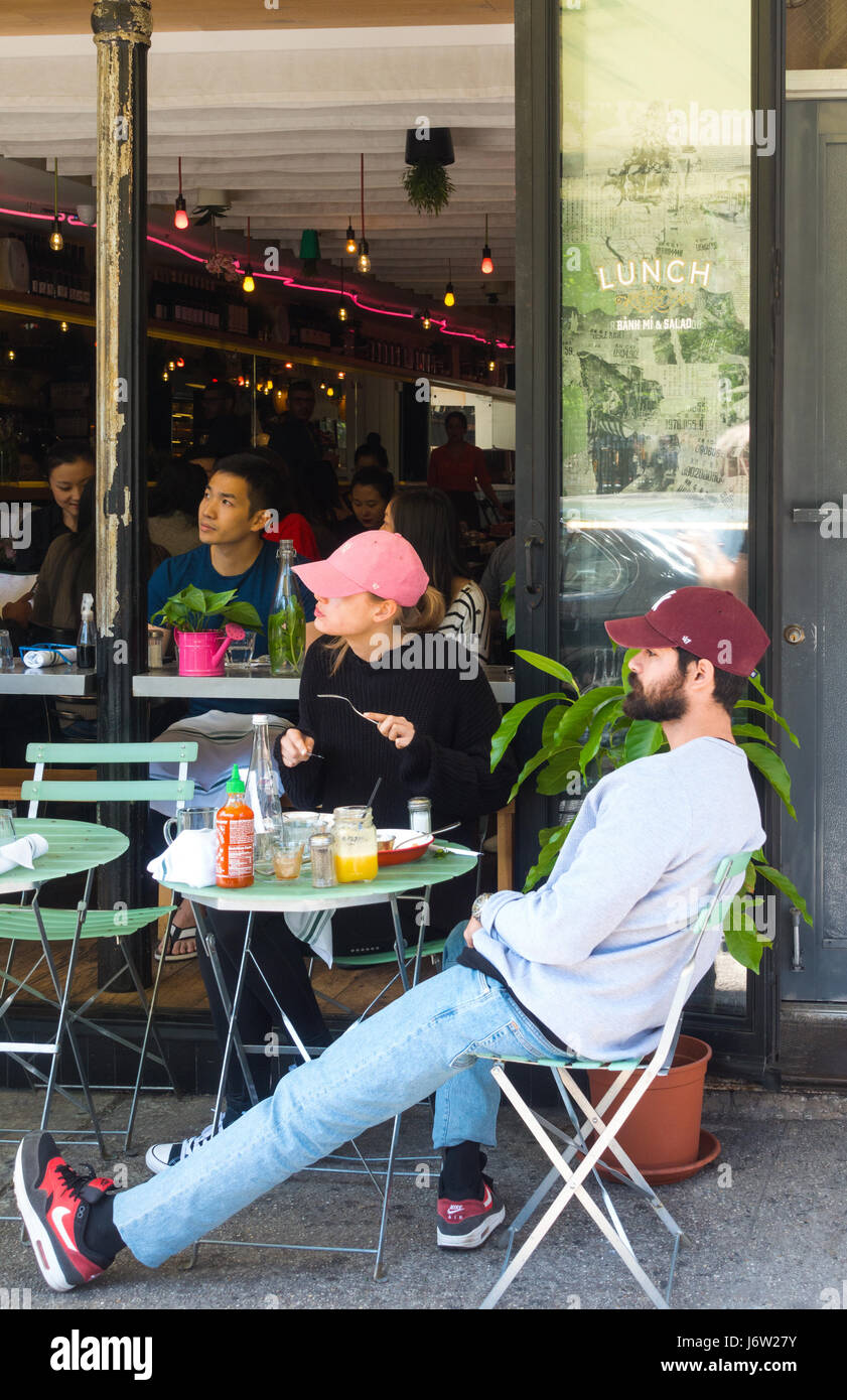 Jeune beau couple de casquettes de baseball de manger à une table à l'extérieur d'un restaurant vietnamien à SoHo, New York City, regardant un travail de construction. Banque D'Images