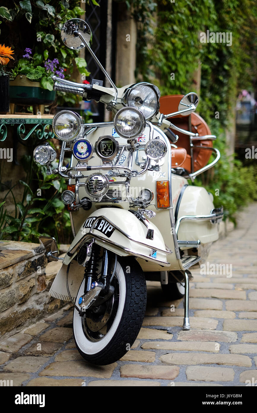 Une rénovation Piaggio Vespa scooter stationné sur une rue pavée contre un bâtiment couvert de plantes. Banque D'Images