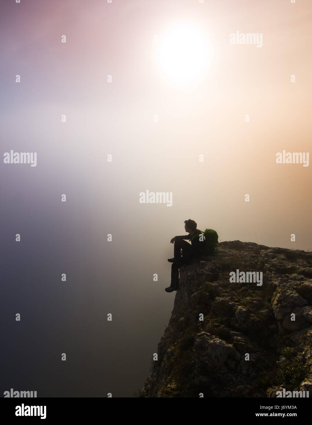 Homme assis sur une falaise par temps brumeux Banque D'Images