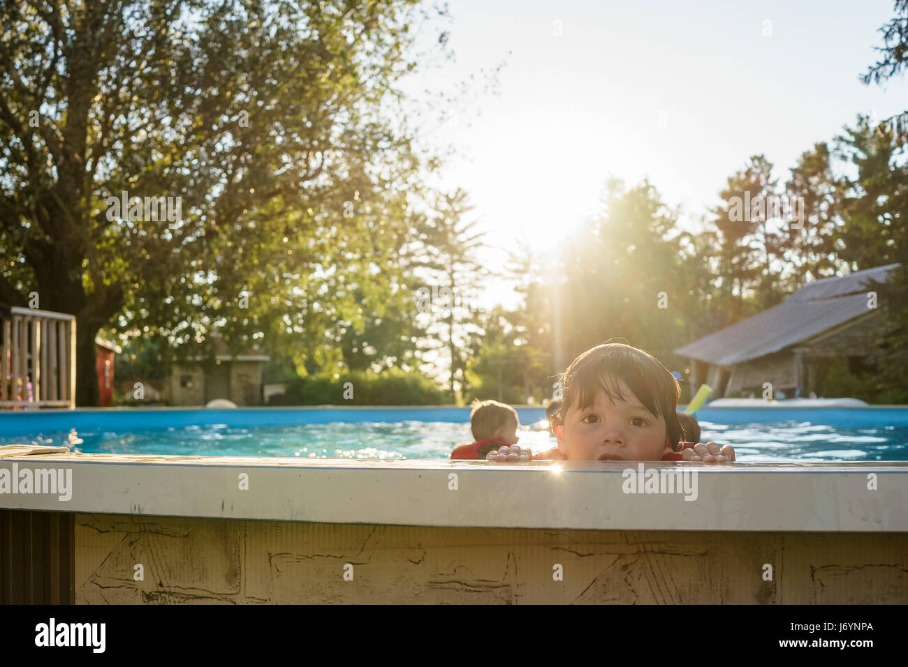 Boy peering over le bord d'une piscine avec les frères et sœurs dans l'arrière-plan Banque D'Images