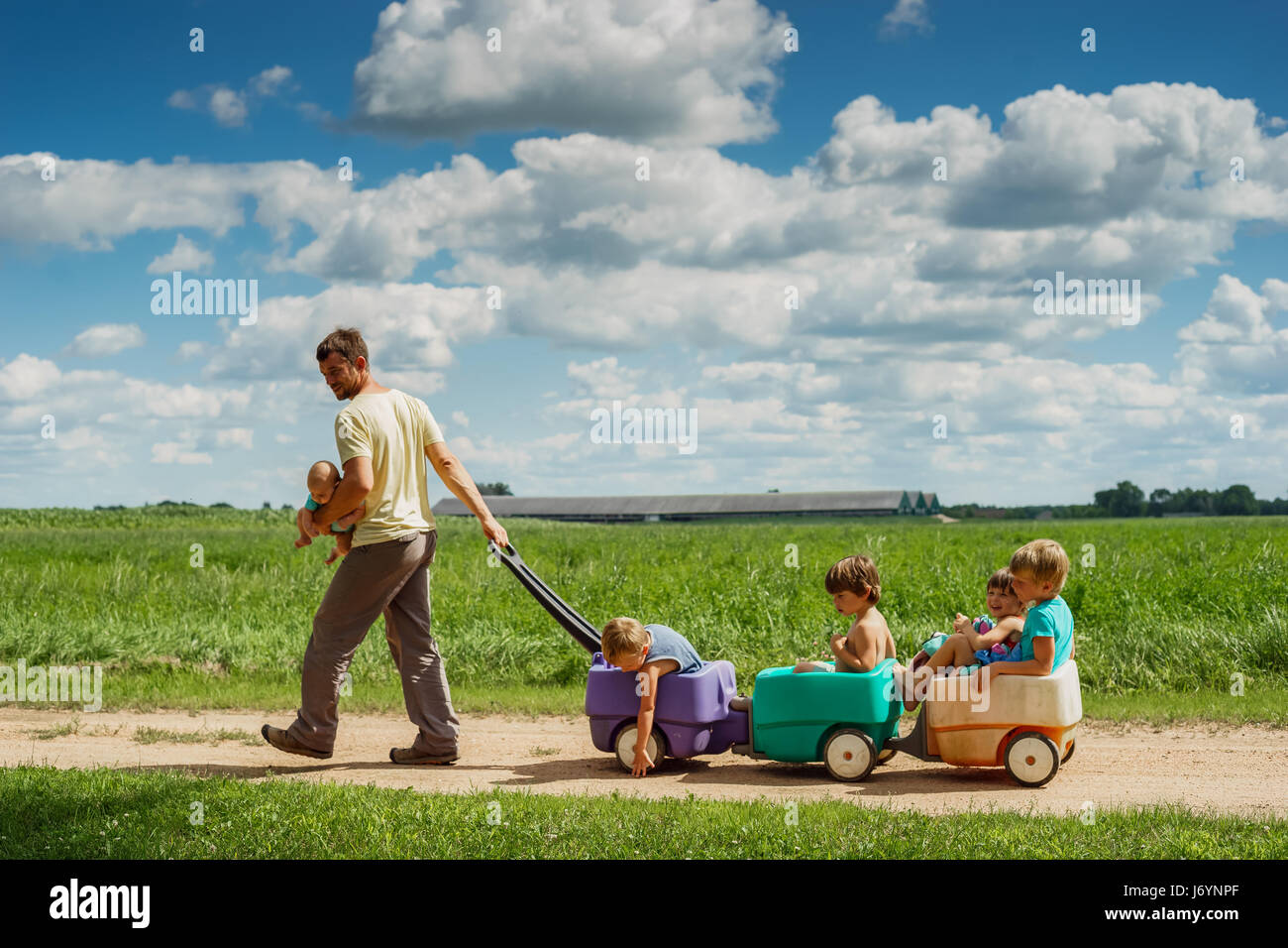 Father carrying baby son tout en tirant quatre enfants dans un chariot Banque D'Images