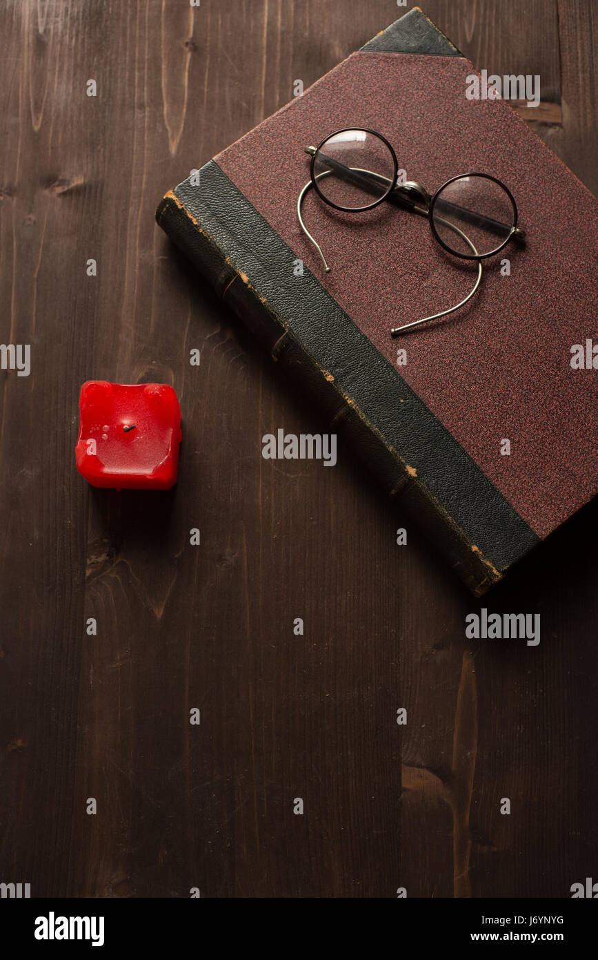 Livre Ancien, une bougie rouge et lunettes sur une table en bois Banque D'Images