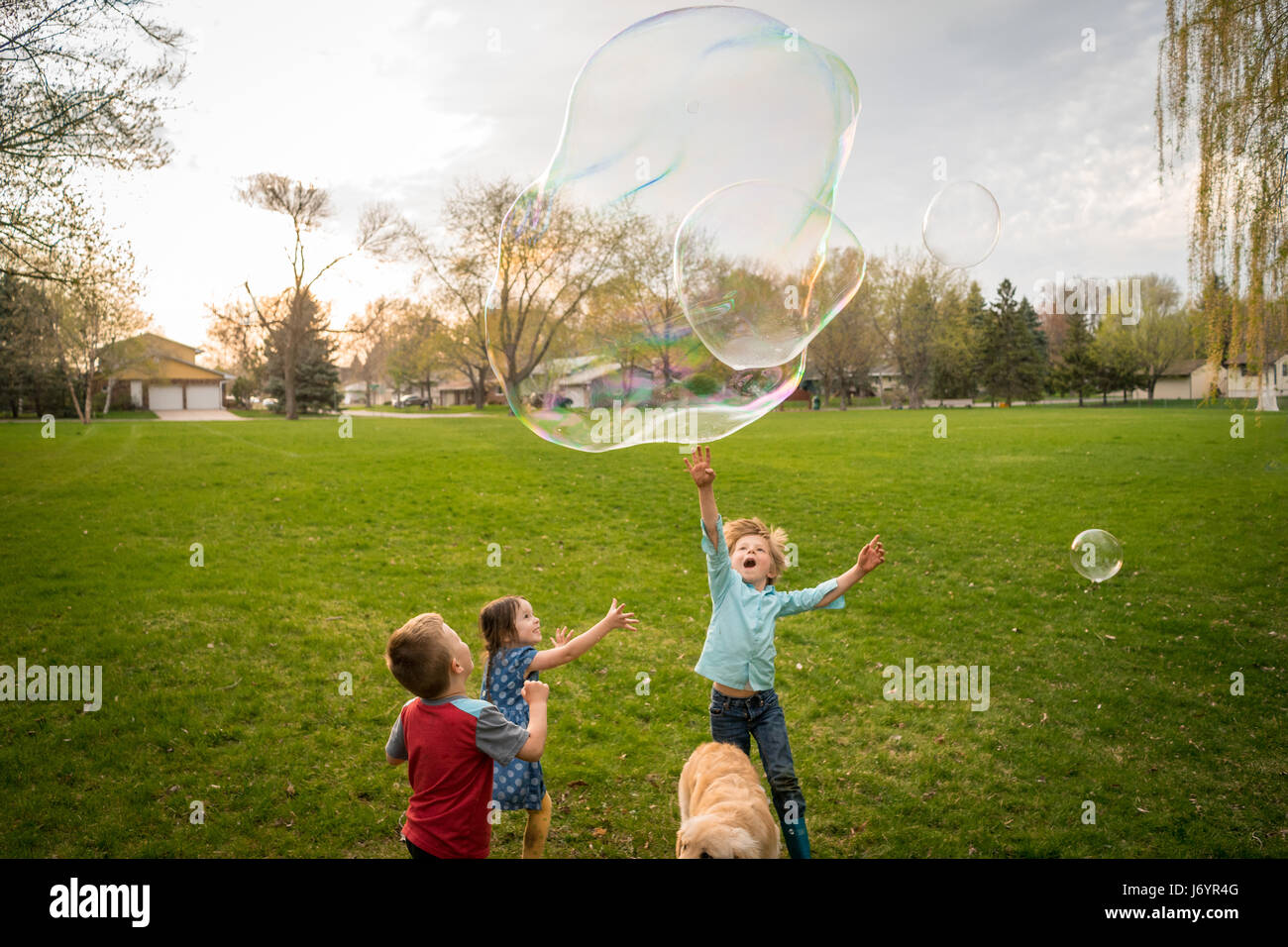 Trois enfants jouant avec des bulles de savon géantes Banque D'Images