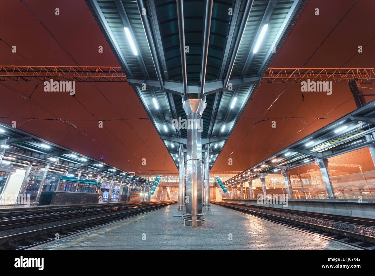 La gare futuriste moderne à l'allumage dans le brouillard pendant la nuit en Europe. Paysage industriel étonnant avec la plate-forme ferroviaire, chemin de fer, ciel, ville Banque D'Images