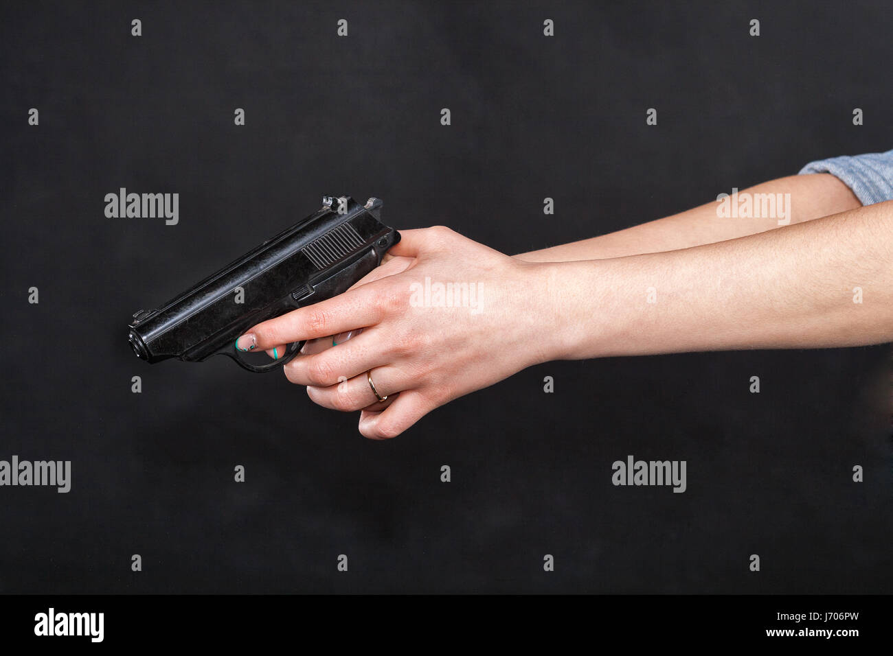 Les femmes de race blanche les bras tendus tenant un pistolet noir, doigts sur la gâchette. Sur fond noir. Banque D'Images