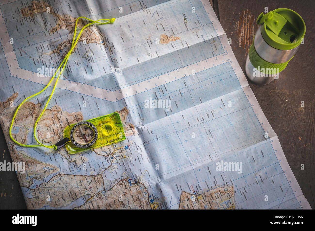 Boussole jaune fluorescent situé sur la carte de îles Lofoten, Norvège sur table en bois à côté de l'argent mug thermique Banque D'Images