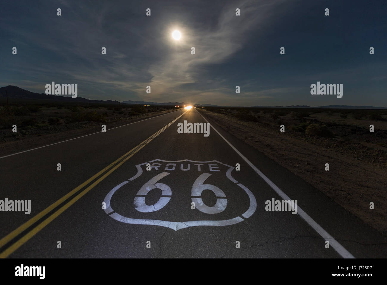 Signer avec Route 66 pleine lune et projecteurs venant en sens inverse dans le désert de Mojave en Californie. Banque D'Images