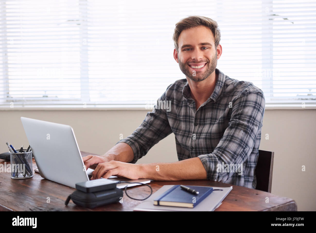 Young male student smiling at camera tout en travaillant sur la cession Banque D'Images