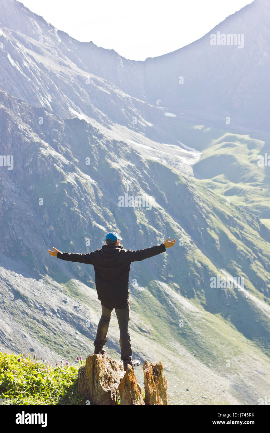 Veste homme en noir debout sur la pierre avec les mains au-dessus de mountais au coucher du soleil Banque D'Images