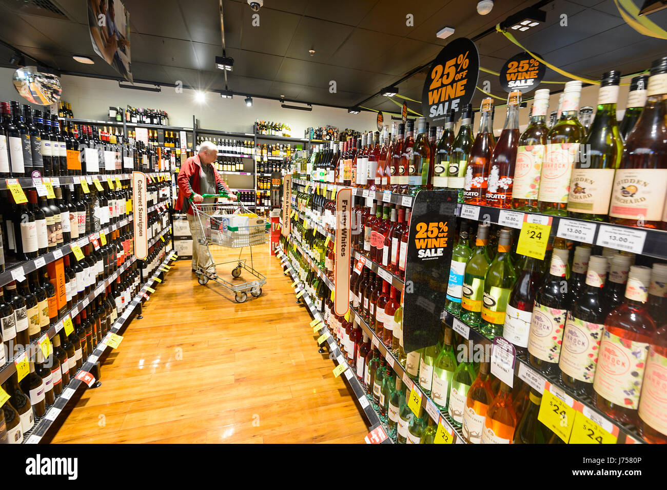 Client avec un panier à la recherche sur les lignes de bouteilles de vin à vendre à BWS Bouteille Boutique, Kiama, New South Wales, NSW, Australie Banque D'Images