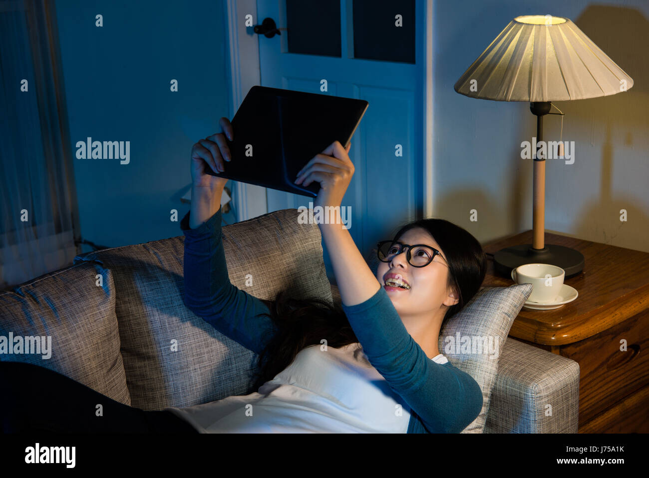 Smiling business dame regardant célèbre film vidéo holding pad ordinateur couché sur la table de nuit près de lampe dans les vacances de détente du soir sans Banque D'Images