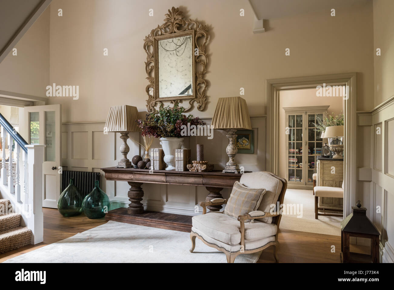 Fauteuil de style français et français paire de bouteilles en verre vert extra large dans le couloir avec une grande table console par Bardoe & Appel. Les murs sont peints en S Banque D'Images