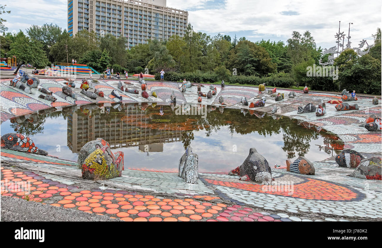 Sur la rive d'un petit étang, parmi les maisons se trouve la sculpture d'un poisson décorée de mosaïques. Le bord de l'eau bordée de beaux t en céramique Banque D'Images