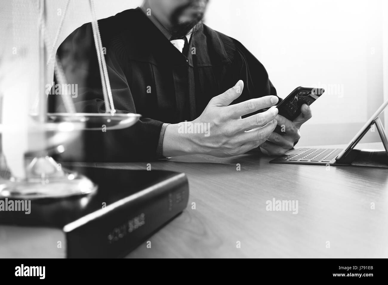 La justice et du droit concept.Homme juge dans une salle d'audience avec le maillet et travailler avec smart phone et l'échelle en laiton sur bois tableau noir et blanc, Banque D'Images