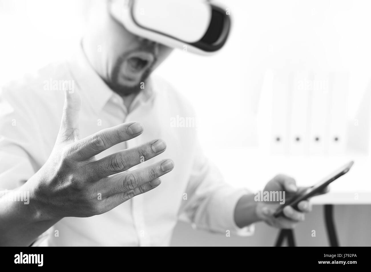 Businessman wearing lunettes de réalité virtuelle dans un bureau moderne avec téléphone portable à l'aide de casque VR avec noir et blanc, Banque D'Images
