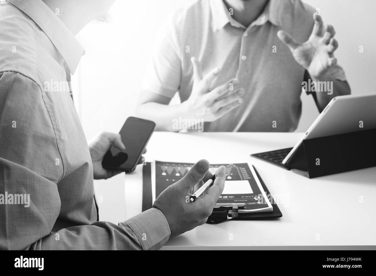 Les hommes d'affaires de travailler ensemble sur un document et à l'aide de smart phone et tablette numérique et votre ordinateur de bureau moderne en noir et blanc, Banque D'Images