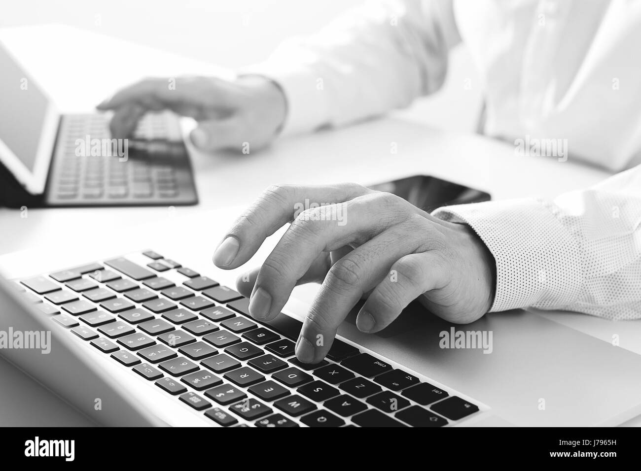 Close up of businessman typing tablette avec clavier numérique et un ordinateur portable sur un bureau blanc bureau moderne en noir et blanc, Banque D'Images