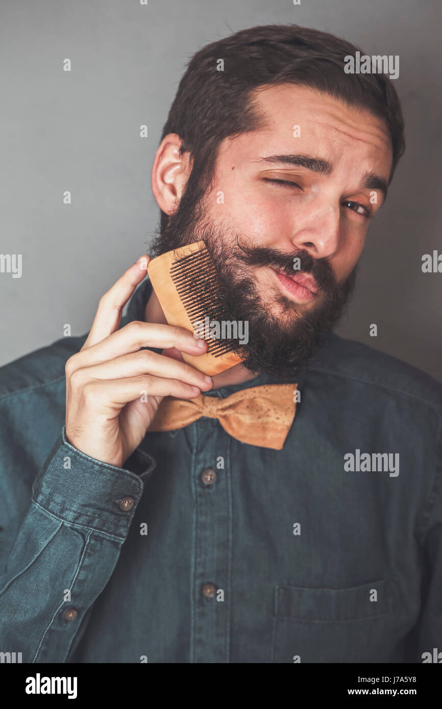 L'homme se peigner sa barbe avec un peigne en bois, portant chemise en jean  et le liège Bow Tie Photo Stock - Alamy