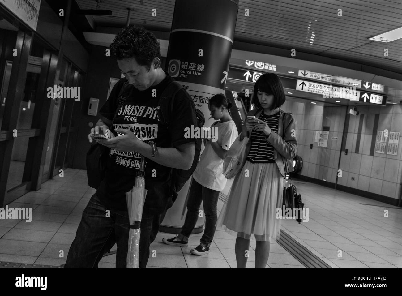 Photo noir et blanc de gens debout à l'intérieur de la station de métro de Tokyo, avec leurs têtes pendant vers le bas comme ils vérifier leurs téléphones mobiles. Banque D'Images