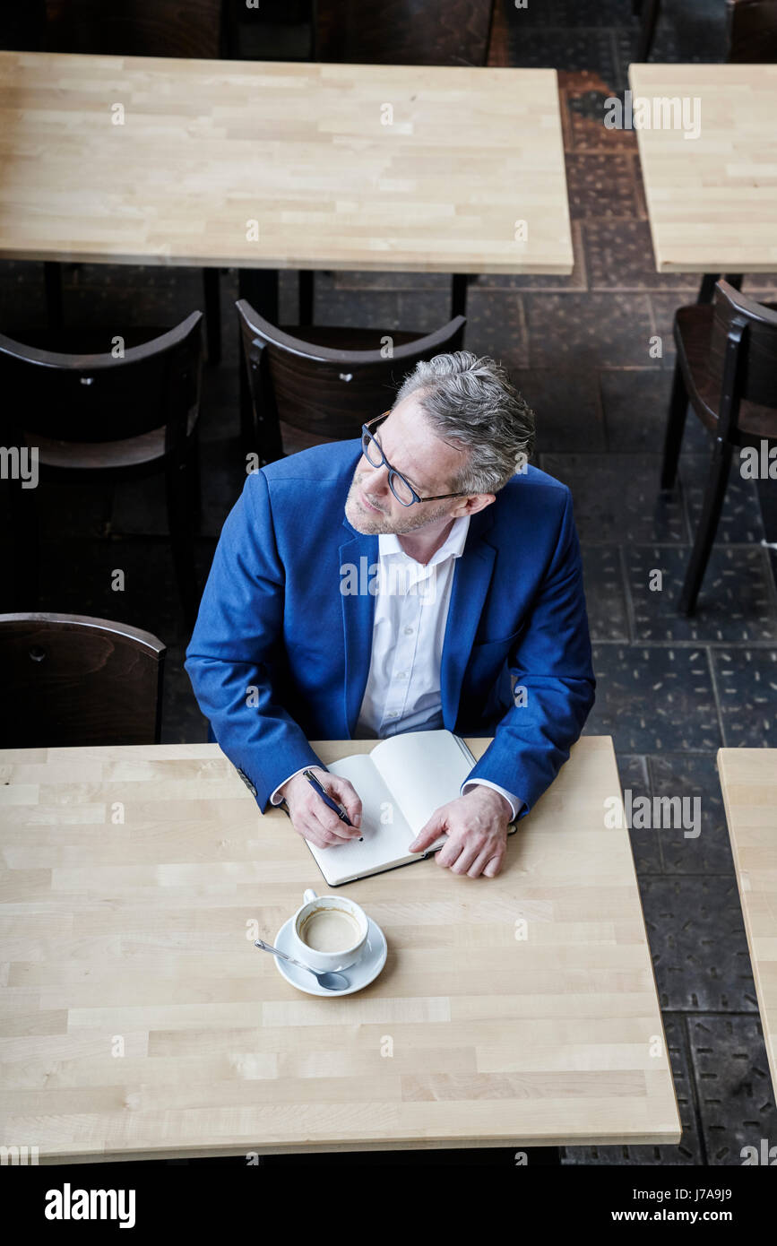 Mature businessman in cafe écrit dans journal Banque D'Images