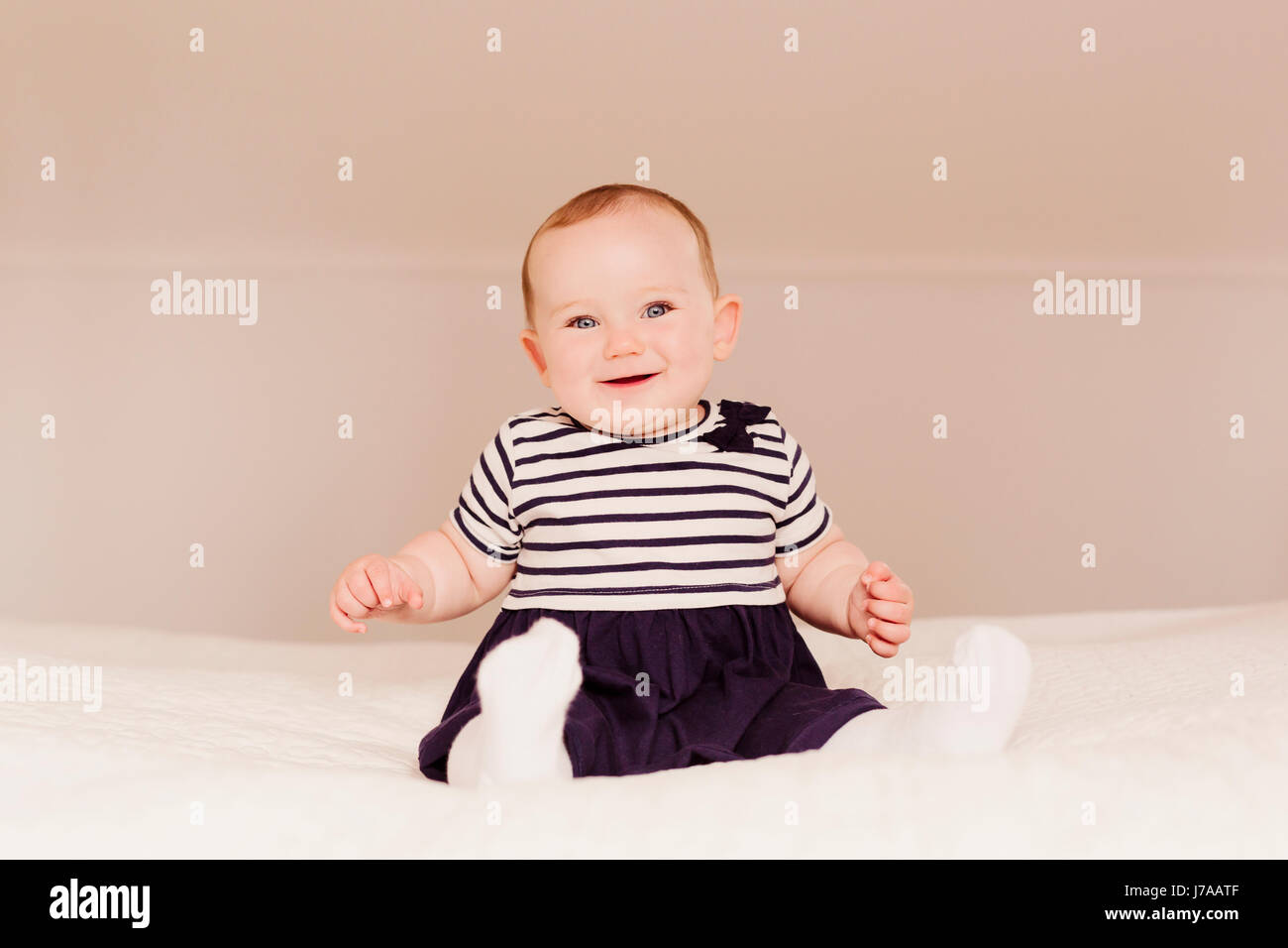 Portrait of smiling baby girl sitting on bed Banque D'Images