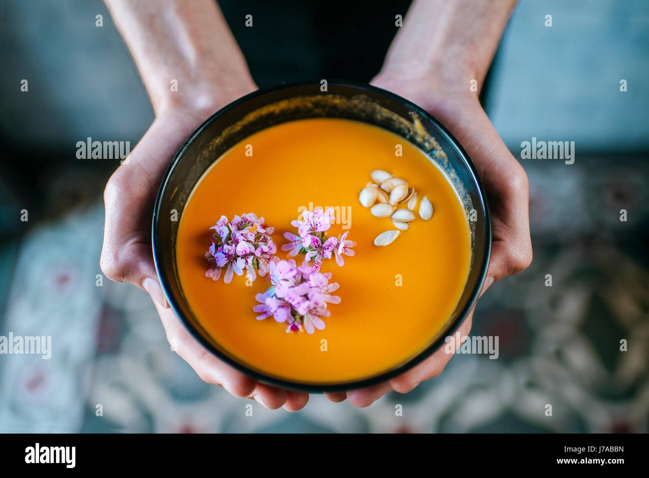 Man's hands holding soupe de potiron à la crème garnie de fleurs comestibles, close-up Banque D'Images