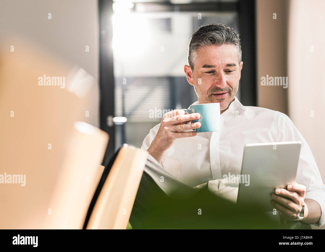 Portrait of businessman avec tasse de café assis à son bureau à l'aide de tablet Banque D'Images