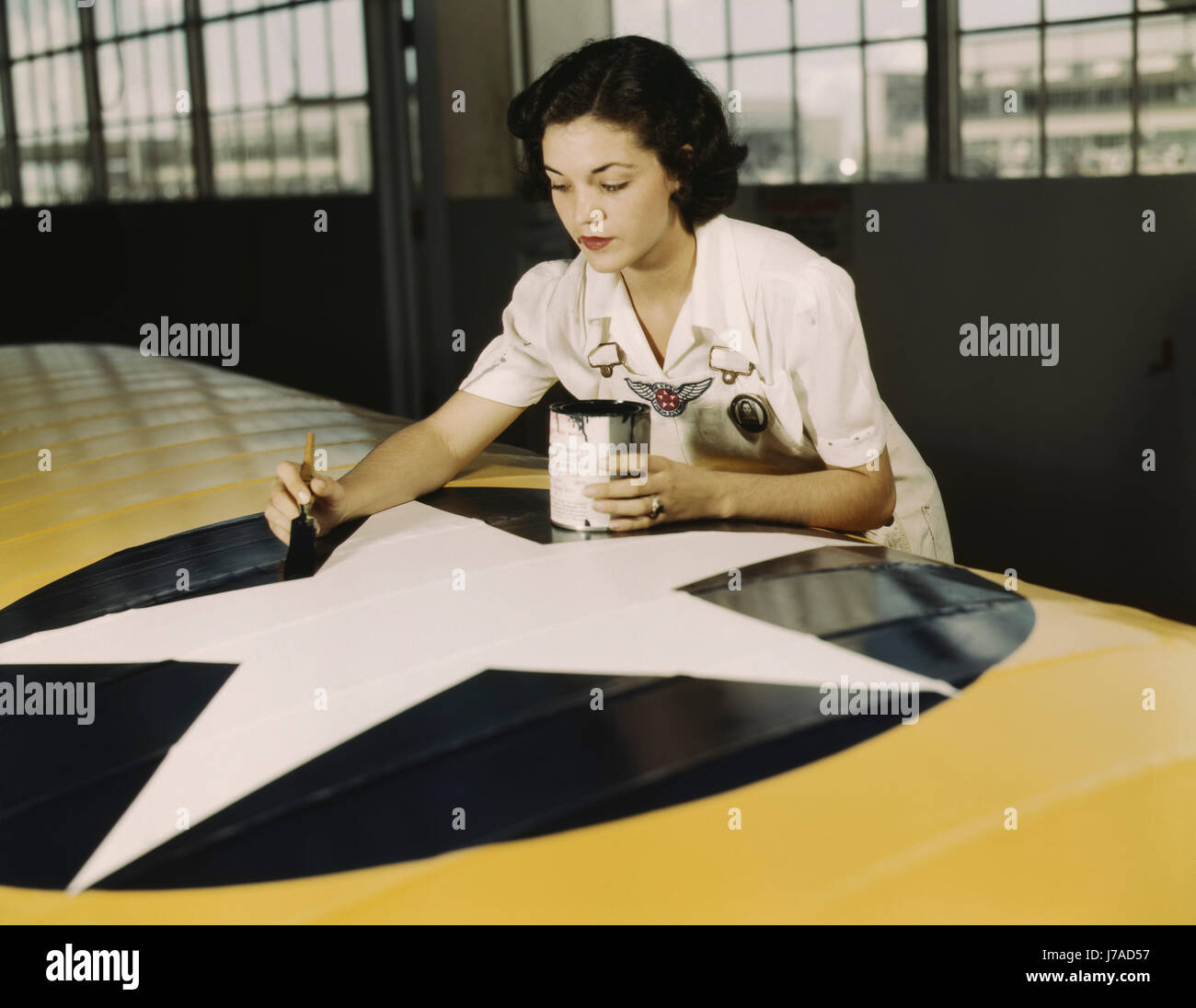 Un travailleur féminin peint l'insigne de la Marine américaine sur une aile d'avion, 1942. Banque D'Images