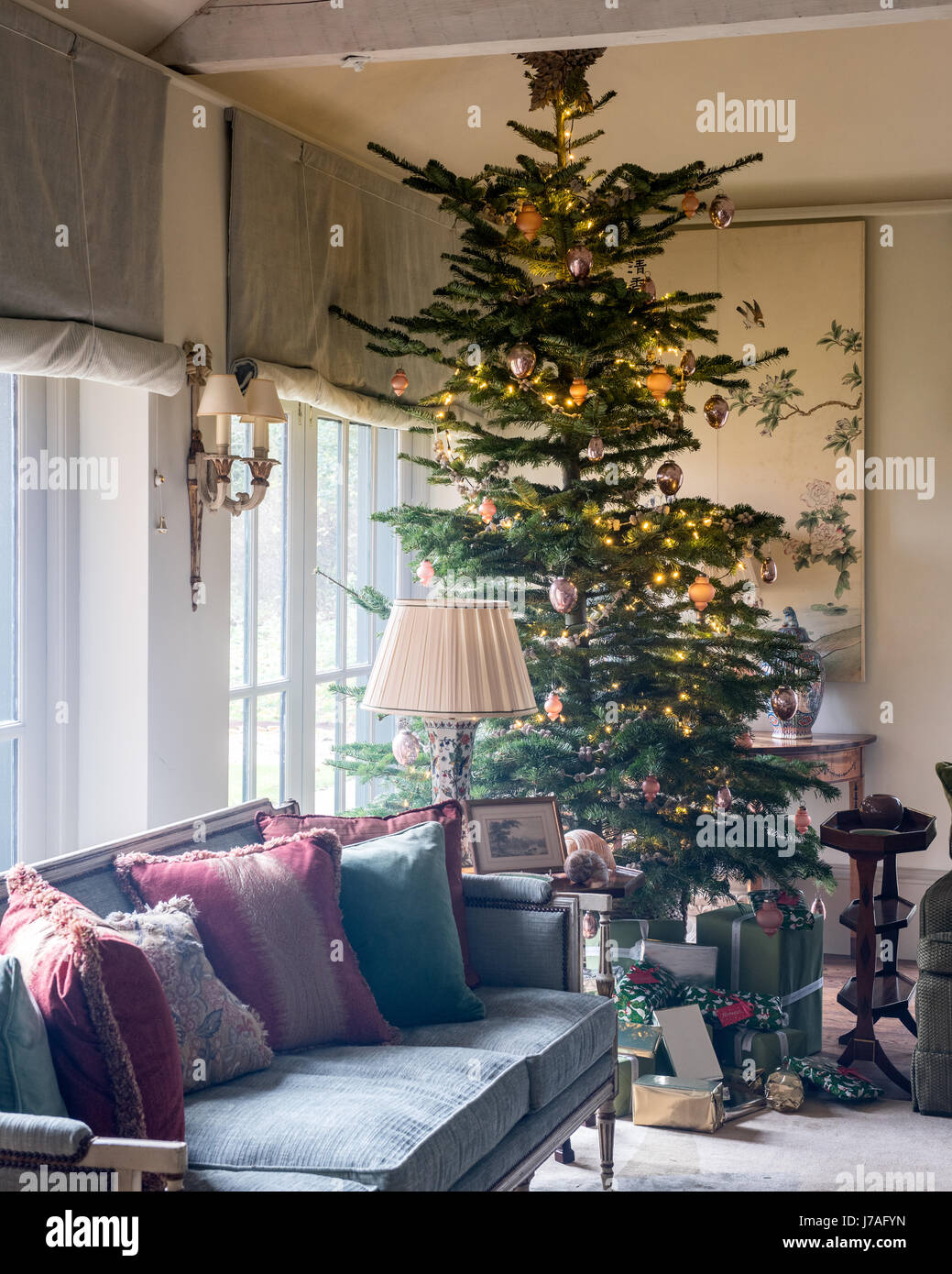 Grand arbre de Noël en coin de salon spacieux avec canapé et panneaux peints chinois ancien. Le canapé d'ameublement et les stores sont de Colefax et Banque D'Images