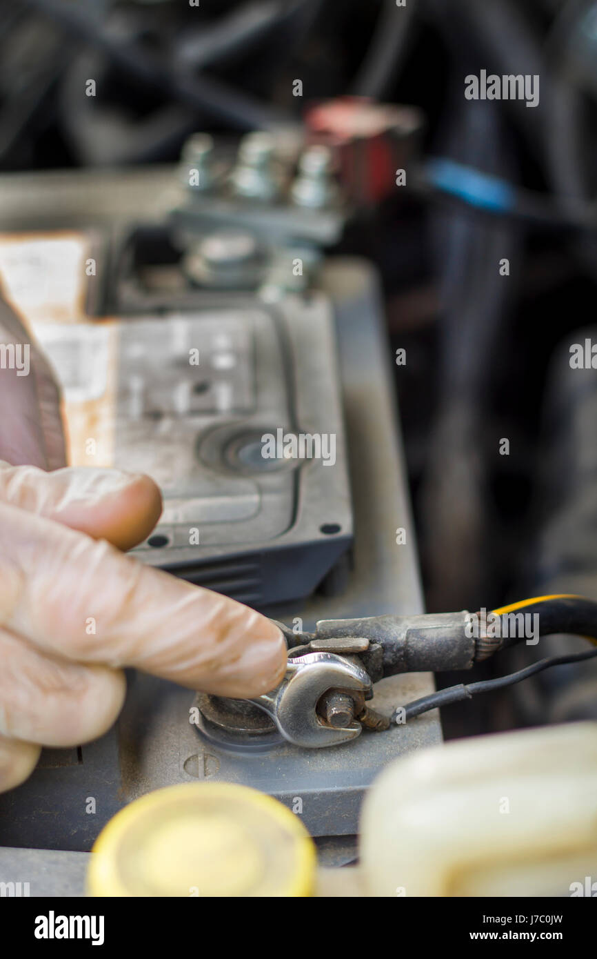 Les mains du mécanicien de voiture dans les gants jetables dévisser l'embrayage de la batterie. La part d'un mécanicien avec une clé plate se dévisse la batterie dans la voiture. Banque D'Images