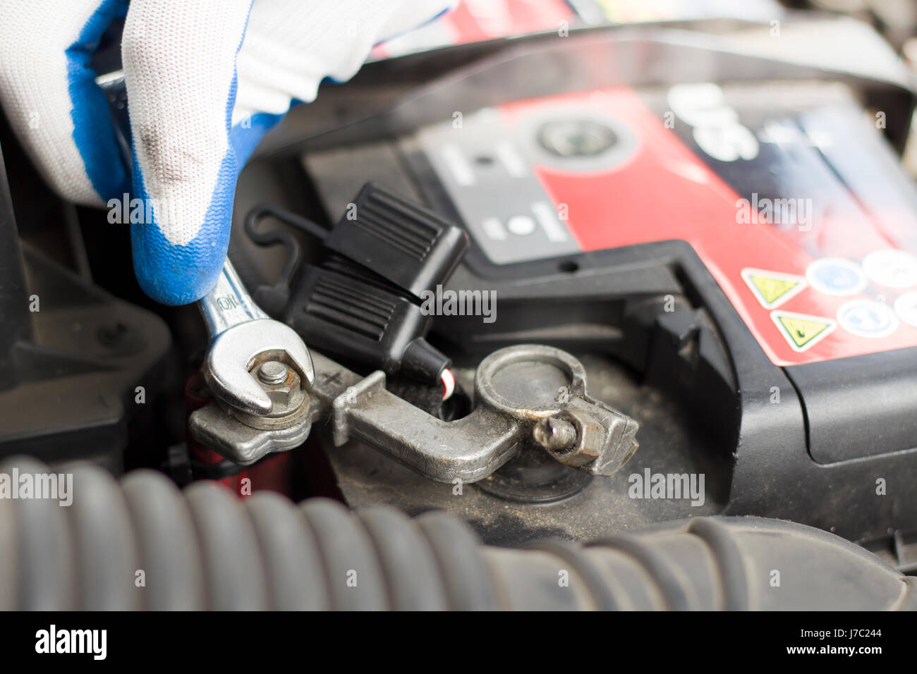 Les mains du mécanicien de voiture dans les gants jetables dévisser l'embrayage de la batterie. La part d'un mécanicien avec une clé plate se dévisse la batterie dans la voiture. Banque D'Images