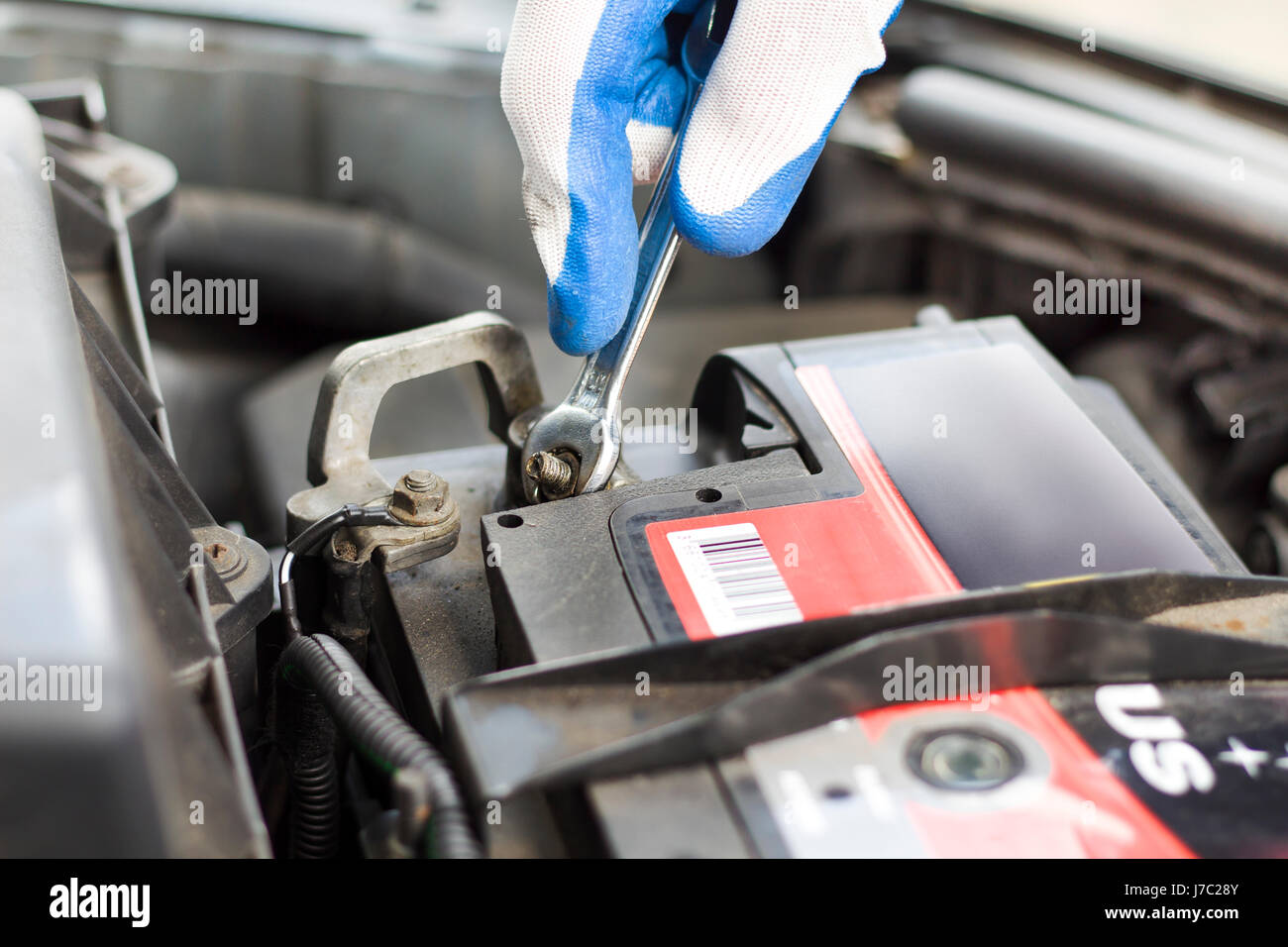Les mains du mécanicien de voiture dans les gants jetables dévisser l'embrayage de la batterie. La part d'un mécanicien avec une clé plate se dévisse la batterie dans la voiture. Banque D'Images